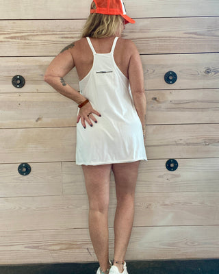 Person wearing a white dress and orange cap against a wooden wall.