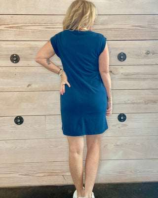 Woman wearing a blue dress standing against a wooden wall.
