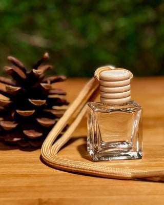 Clear glass diffuser bottle with wooden cap next to a pine cone on a wooden surface