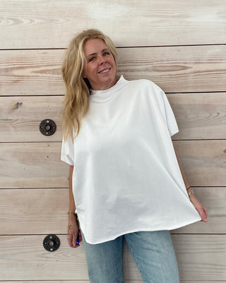 Person wearing a white shirt and blue jeans standing on a wooden floor.