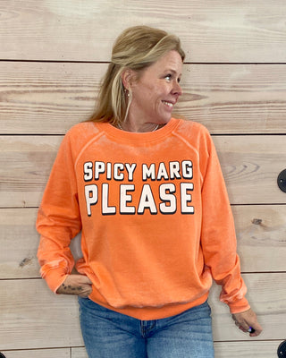 Woman wearing an orange sweatshirt with 'Spicy Marg Please' text against a wooden background