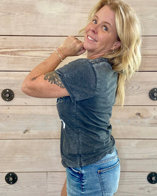 Woman wearing a dark gray t-shirt and blue jeans against a wooden background