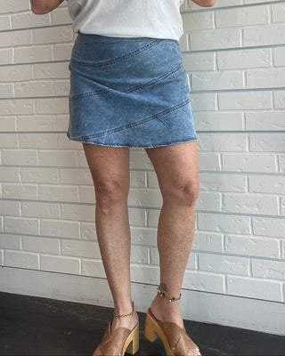 Person wearing a white shirt and denim skirt standing against a tiled wall.