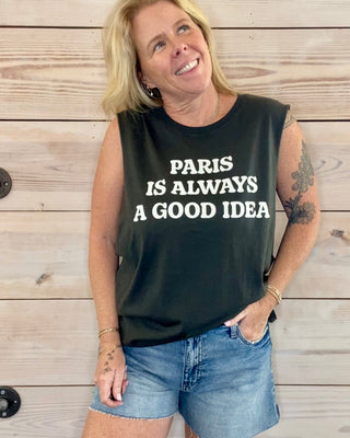 Woman wearing a black sleeveless shirt with 'Paris is Always a Good Idea' text against a wooden background