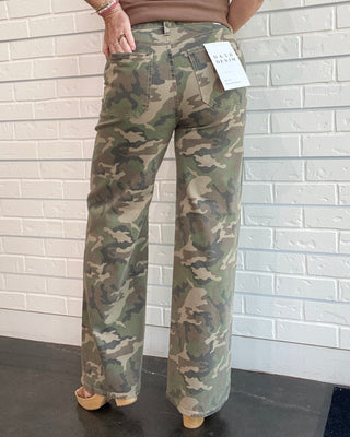 Person wearing camouflage pants with a white brick wall background