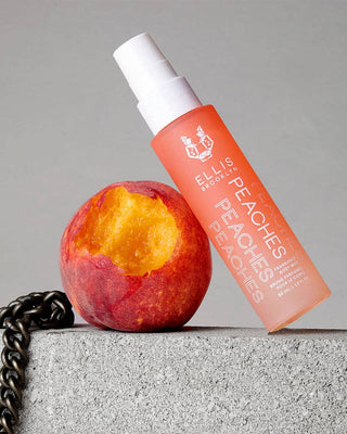 Ellis Brooklyn 'Peaches' perfume bottle next to a peach on a concrete surface with a gray background
