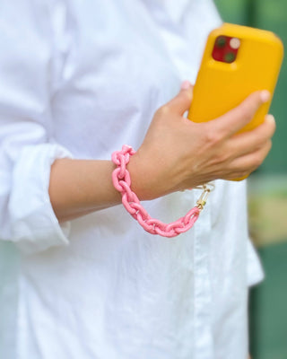 Person holding a yellow phone with a pink bracelet on a blurred background