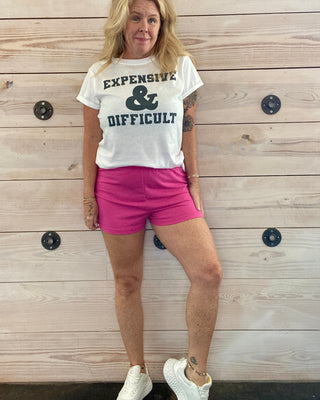 Person wearing a white t-shirt with text and pink shorts standing against a wooden wall.