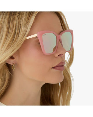 Close-up of a person wearing pink cat-eye sunglasses with a blurred background