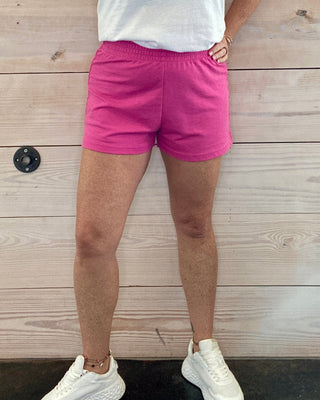 Person wearing a white t-shirt with text and pink shorts against a wooden background
