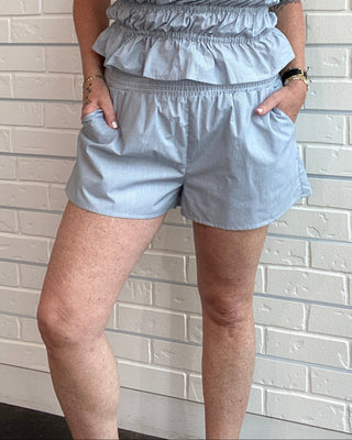 Woman wearing a light blue shorts against a white brick wall.