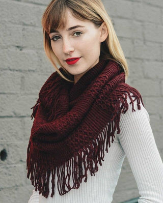 Woman wearing a burgundy knitted scarf against a gray wall.