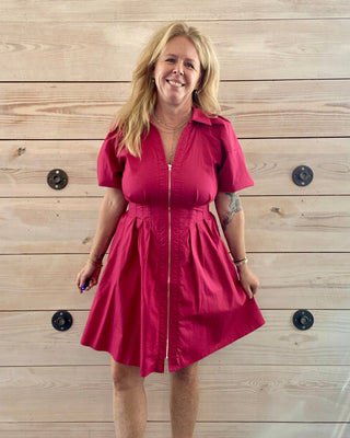 Woman wearing a red dress standing against a wooden wall.