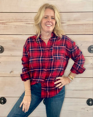 Woman wearing a red plaid shirt and jeans standing against a wooden background