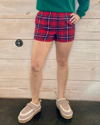 Person wearing a green sweatshirt with text and red plaid shorts against a wooden background