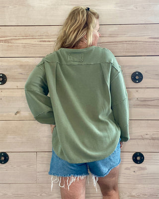 Person wearing a green sweatshirt and denim shorts standing on a wooden floor.