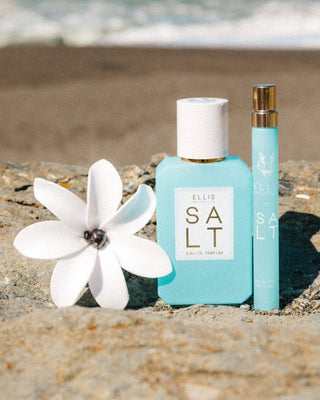 Two bottles of Ellis Salt perfume on a beach with a white flower.