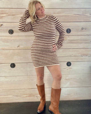 Woman wearing a striped dress and brown boots against a wooden wall.