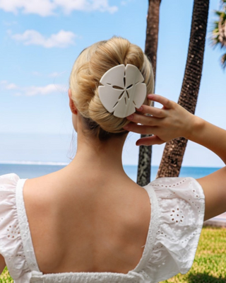 Woman with a sand dollar hair clip with palm trees and ocean in the background