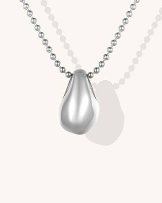 A silver teardrop pendant necklace with a polished metallic finish, suspended from a matching silver ball chain against a light cream background.