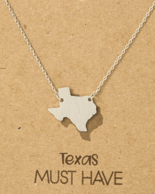 Silver necklace shaped like the state of Texas on a brown card with text.
