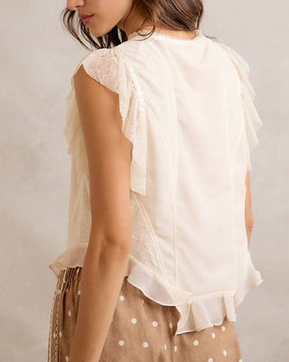 Woman wearing a light-colored blouse with ruffled sleeves against a neutral background