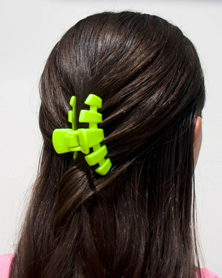 A bright lime green claw clip holding back dark brown hair, shown from the back on a model against a plain white background.