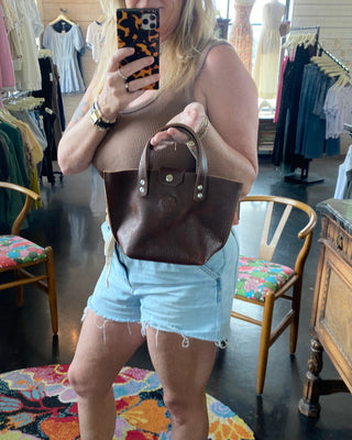 Person holding a brown handbag in a clothing store