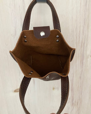 Brown leather bag with a strap on a light wooden surface