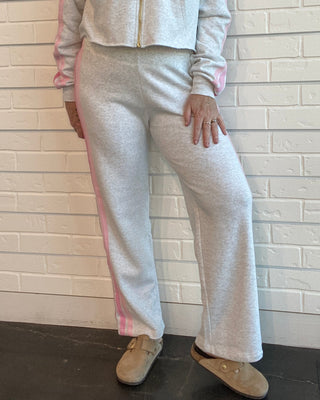 Person wearing a light gray tracksuit with pink accents against a white brick wall.