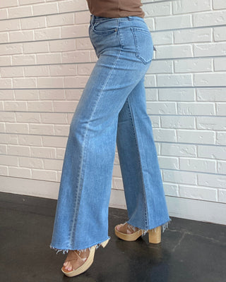 Person wearing a brown top and blue flared jeans against a white brick wall.