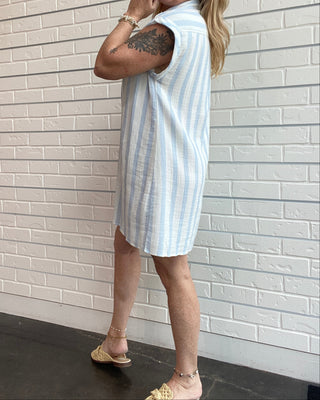 Woman wearing a light blue and white striped dress against a white brick wall.