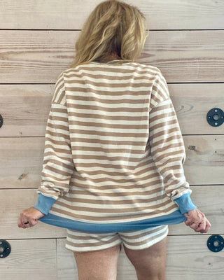 Person wearing a striped shirt and shorts against a wooden wall.