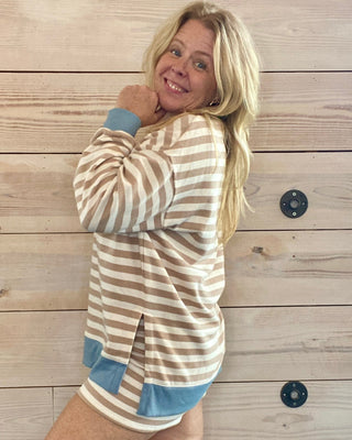 Woman wearing a striped sweater and shorts against a wooden wall.