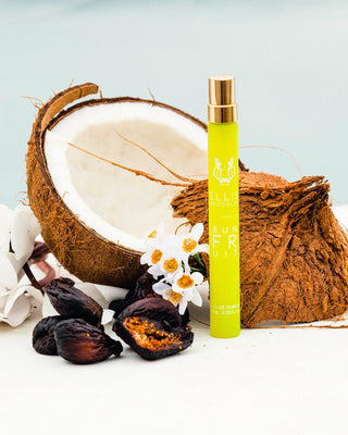 Green perfume bottle with gold cap next to a coconut and dried fruits on a light blue background