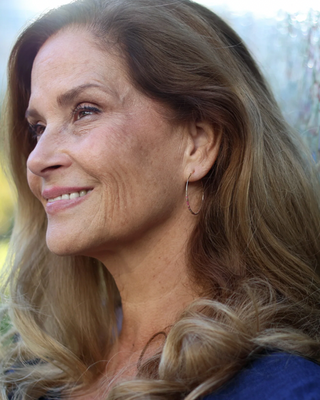 Woman with long blonde hair wearing a blue top outdoors featuring earrings that spell out 'survivor' in morse code.