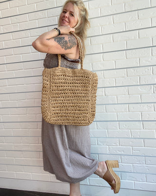 Woman holding a woven bag against a white brick wall