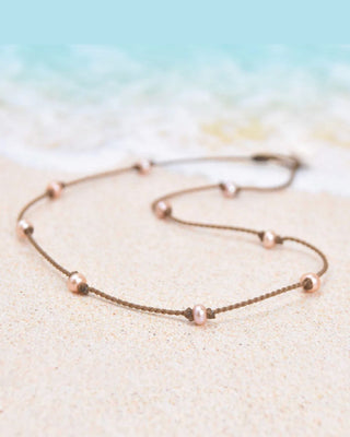 Delicate necklace with small blush pearl beads on a sandy background