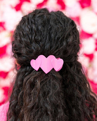 Black hair styled in a braid with pink heart-shaped hair clips against a blurred floral background.