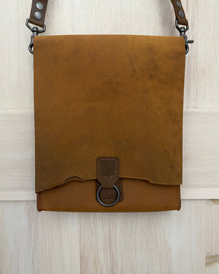 Brown leather bag with strap on a light wooden surface
