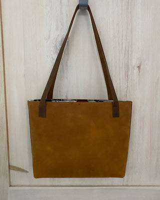 Brown leather tote bag on a light wooden surface