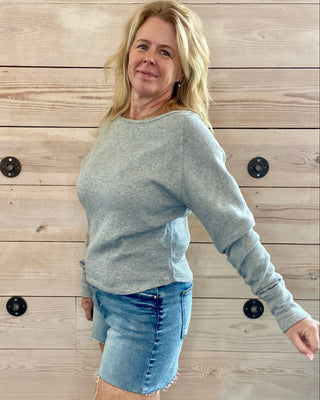 Woman wearing a gray sweater and denim skirt against a wooden wall.