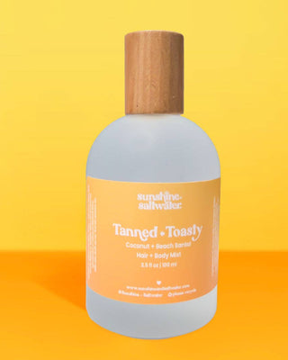 Bottle of 'Tanned & Toasty' hair and body mist with a wooden cap on a yellow background