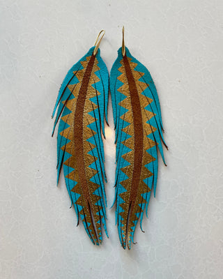 Pair of feather-shaped earrings with blue and brown patterns on a light gray background