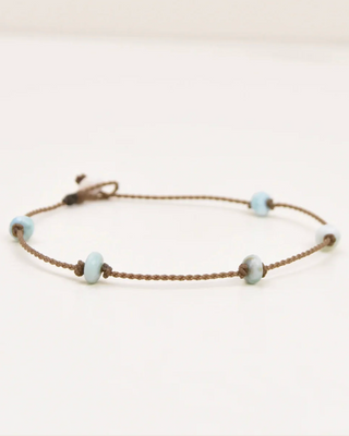 Anklet with small beads on a thin brown cord against a light background
