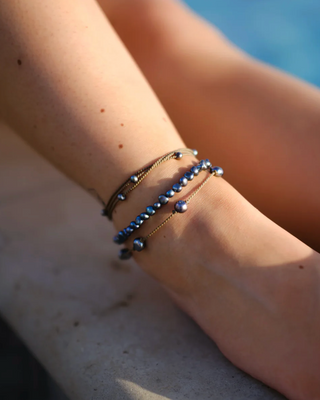 Close-up of a person's ankle with multiple anklets by a poolside.