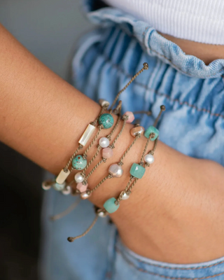 Close-up of a person's wrist wearing multiple beaded bracelets on a blurred background
