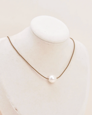 Pearl necklace on a mannequin bust against a plain background