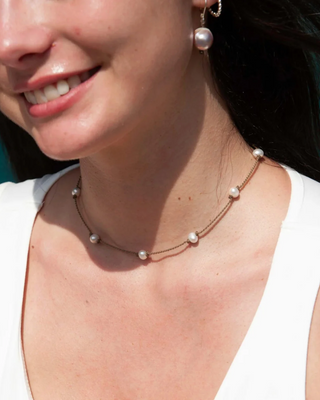 Close-up of a woman wearing a pearl necklace and earrings with a blurred background