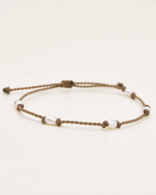 Bracelet with brown cord and white beads on a light beige background